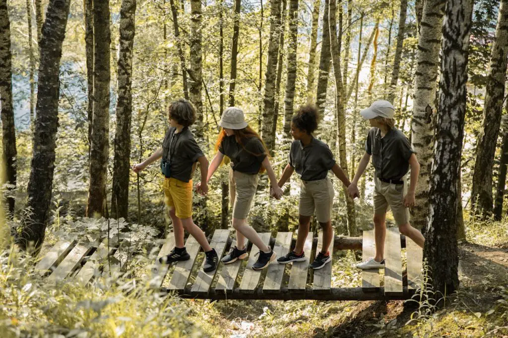 Teenagers Holding Hands While Walking on Wooden Bridge in Forest.