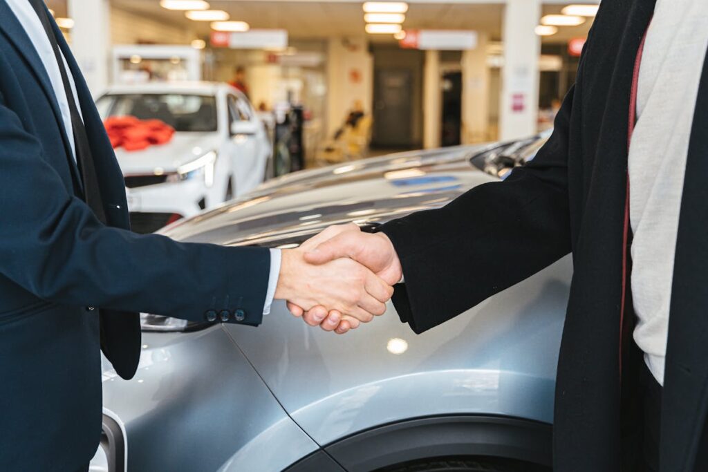 two man shaking hands right next to a car