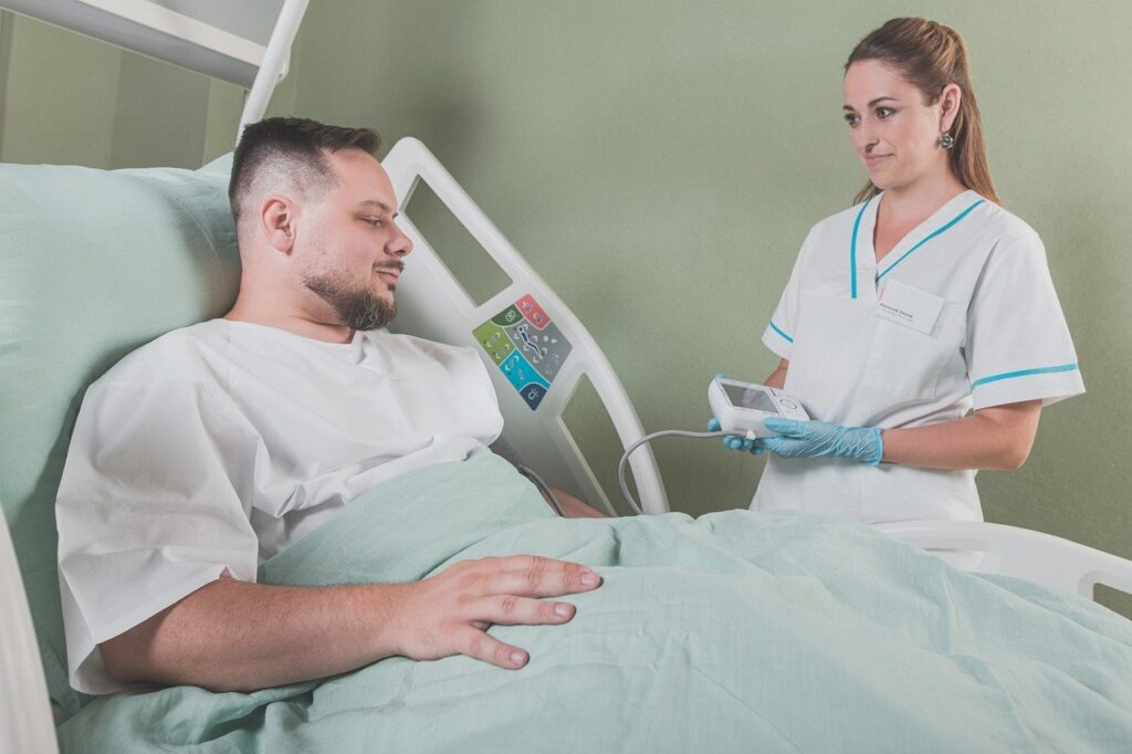 A male patient in a hospital bed being cared for by a nurse.